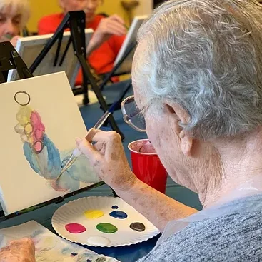 An older man painting a bunch of grapes at his easel