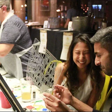A couple laughing as they paint together at an evening workshop