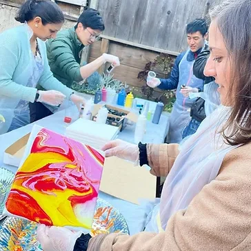 A team pouring bright paint onto canvases at an outdoor table