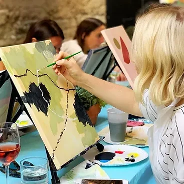 A woman painting a leafy branch on her canvas, a glass of rosé beside her