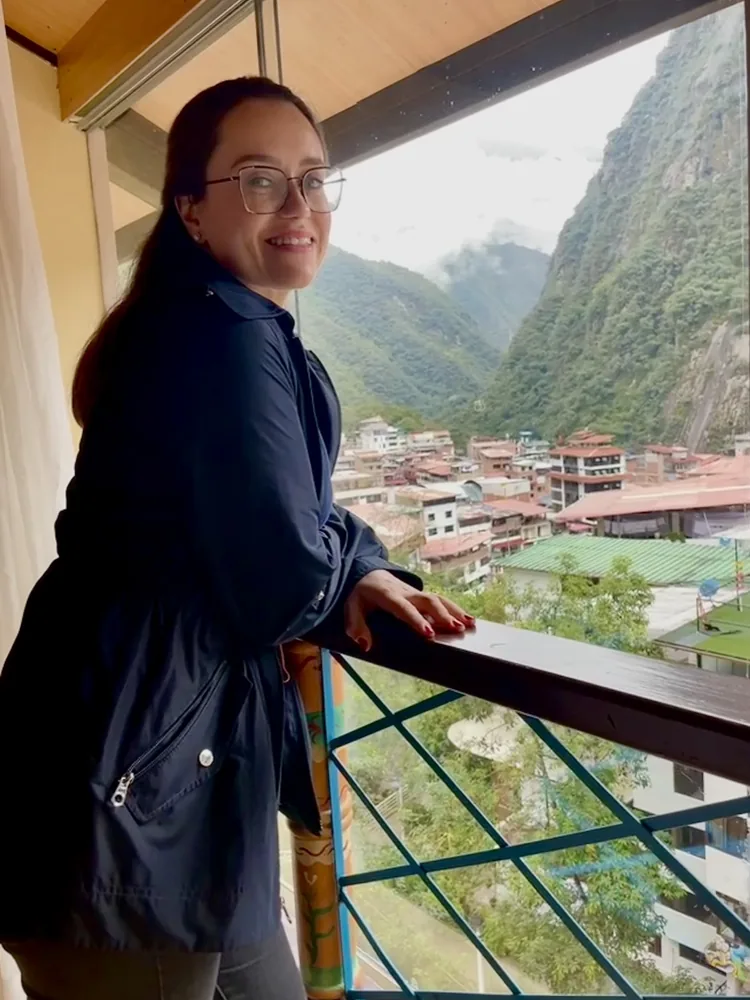 Ana smiling on a balcony above a town in steep green mountains