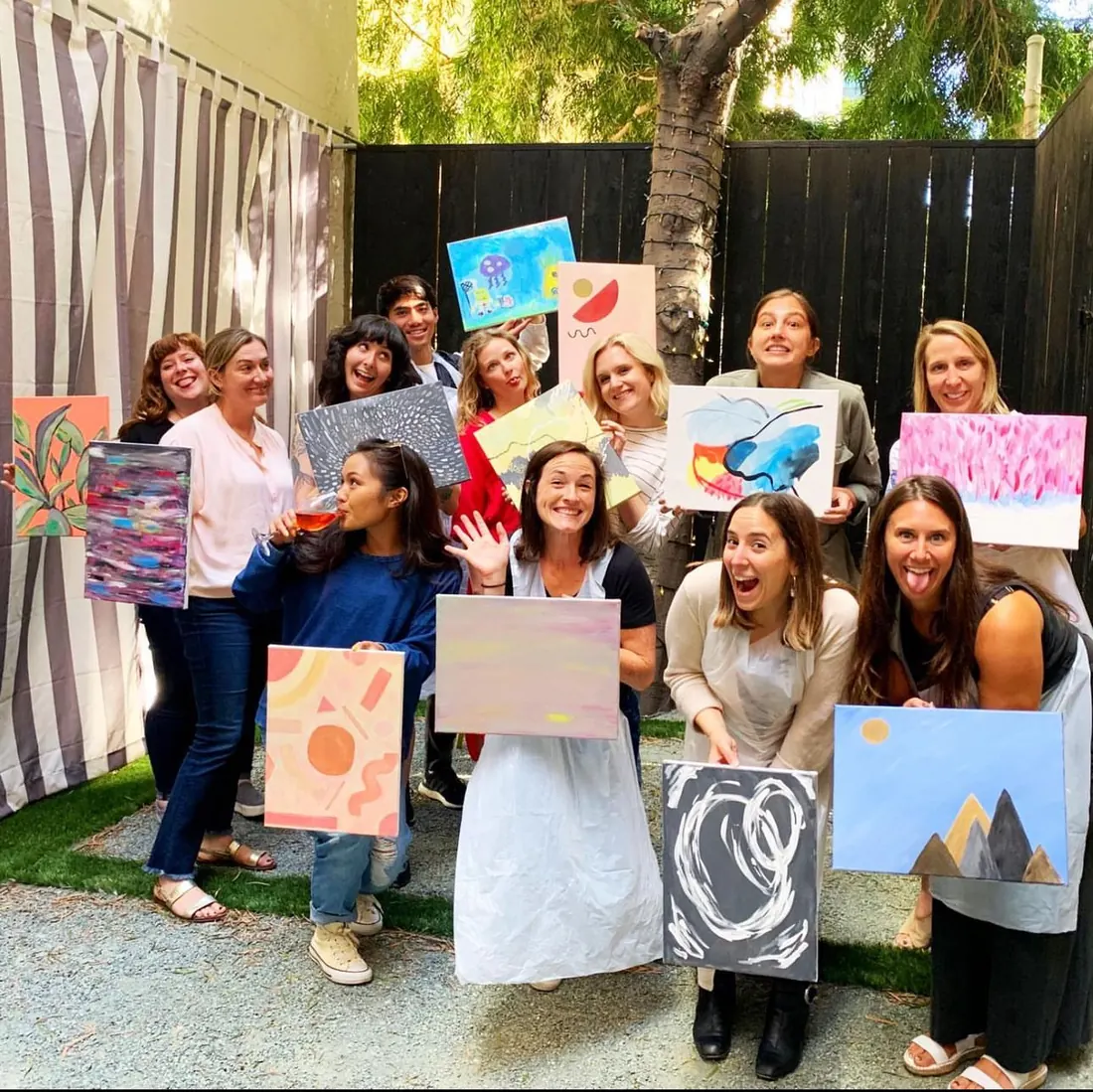 A group of women laughing and holding up the paintings they made at one of Ana's workshops
